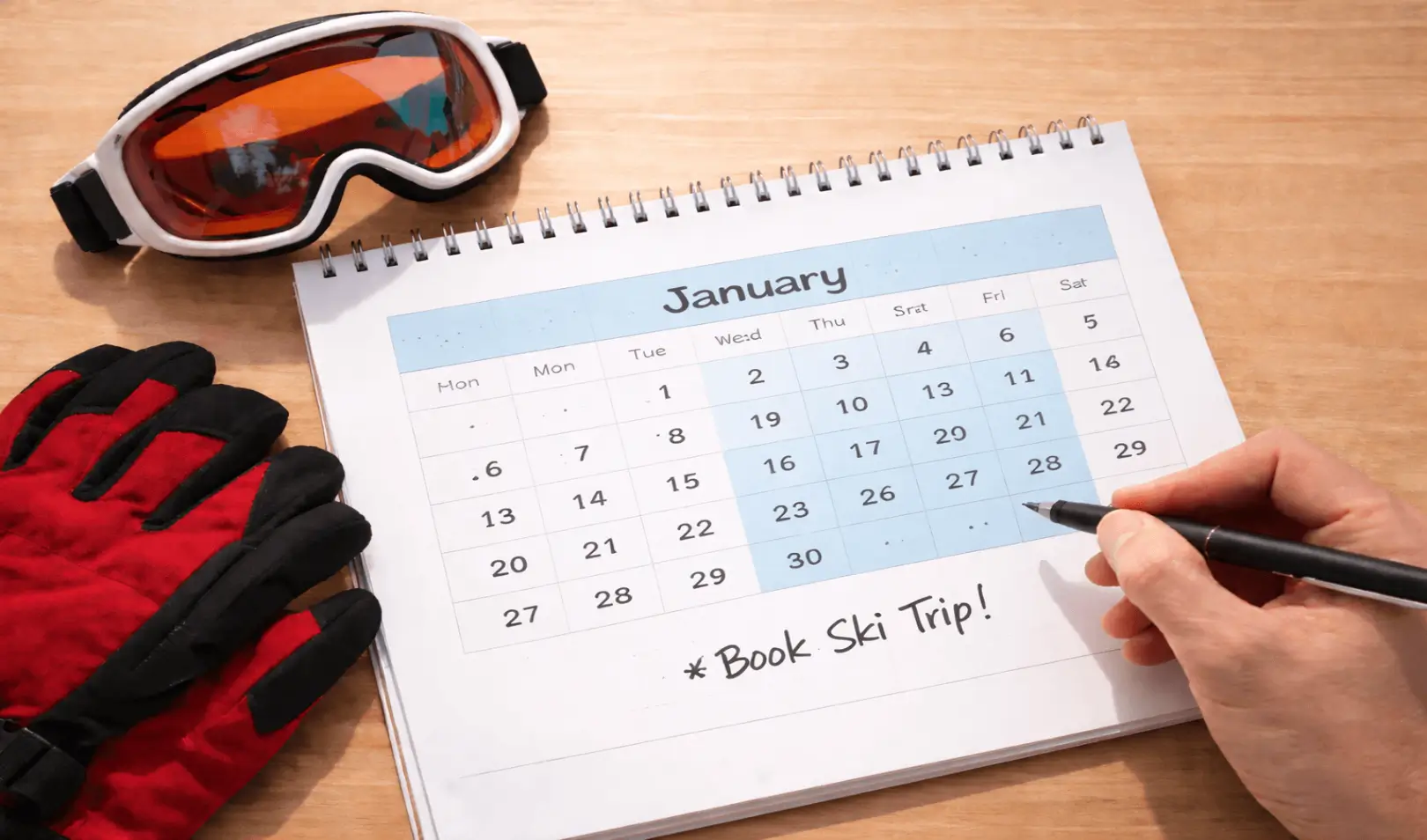 Kalendar za siječanj s označenim datumima, skijaške rukavice i naočale na stolu te bilješka “Book Ski Trip” kao planiranje zimskog putovanja